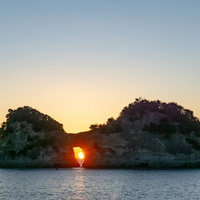 円月島の穴に沈む夕陽と海に反射するオレンジの光の写真