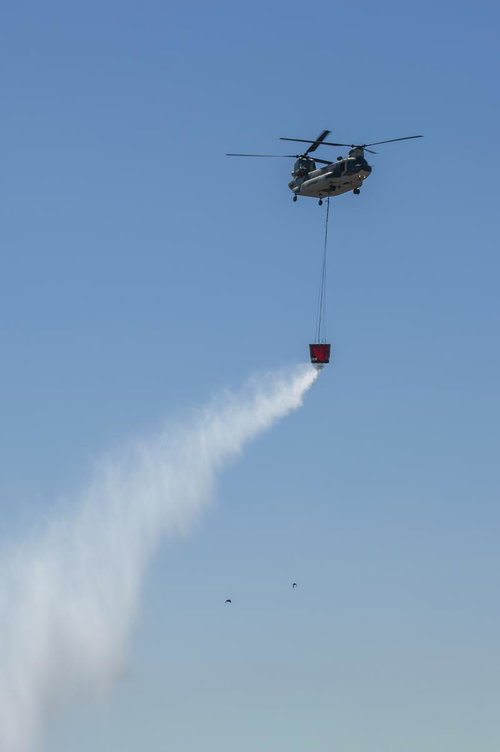 ワイヤーで吊り下げた消火バケットから放水デモを行うCH47の様子