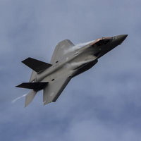 柔らかな雲が浮かぶ空を肩口からベイパーを出して機動飛行を行うF35の姿の写真