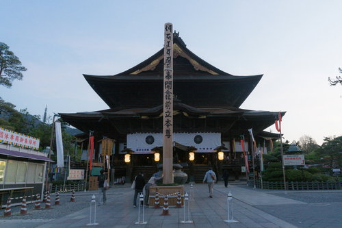 夜明け直後の善光寺本堂前に立つ回向柱と灯る燈明